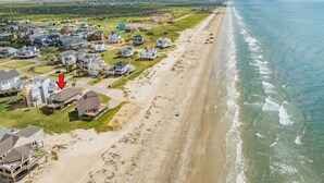 Vue aérienne d’une zone résidentielle côtière, avec des maisons le long de la plage, un ciel dégagé et une mer calme.