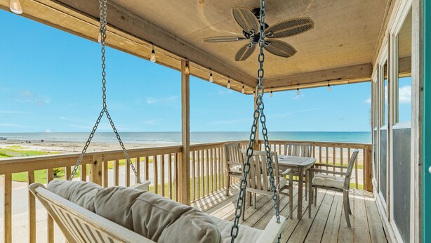 Une terrasse en bois avec une balançoire, une table et des chaises, donnant sur une plage.