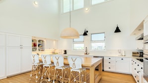 Una cocina amplia con armarios blancos, una isla de madera con taburetes altos y un gran ventanal que proporciona luz natural.