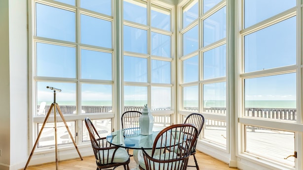 Comedor con mesa de vidrio y sillas de madera, ventanas amplias con vista al océano y al muelle.