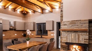 Eine moderne Küche mit Holzbalken, einem Kamin aus Stein und einem Essbereich mit Stühlen und Tisch.