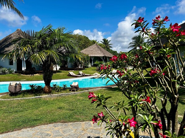 A pool area with lounge chairs, a thatched-roof structure, and lush greenery. - Duna Paraiso Maceió (Maceio)
