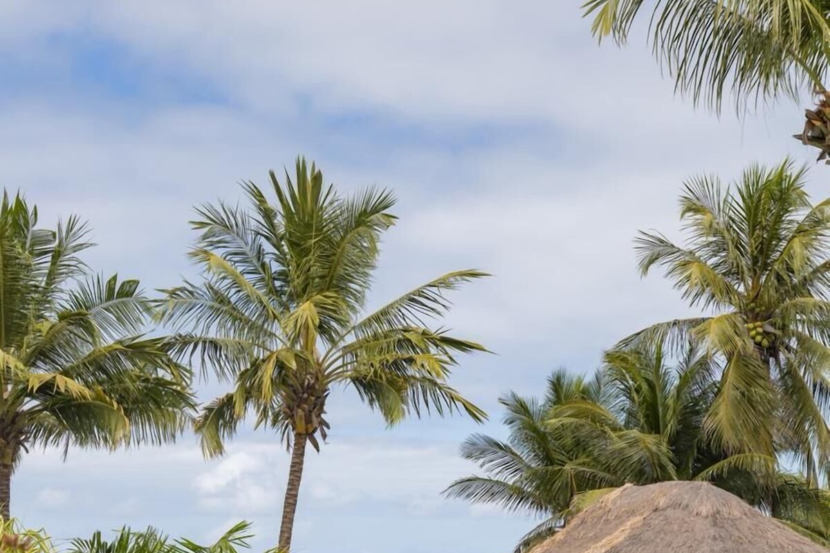 A pool area with lounge chairs, a thatched-roof structure, and palm trees.