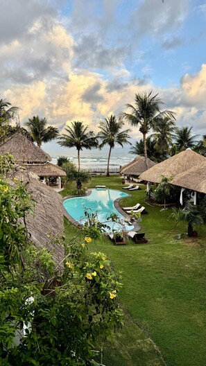 A pool area with thatched-roof structures, palm trees, and a view of the ocean. - Duna Paraiso Maceió (Maceio)