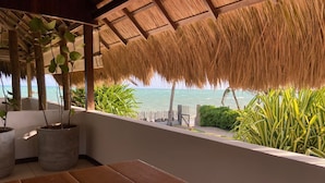 Een houten bank, potplanten, een rieten dak en uitzicht op de zee.