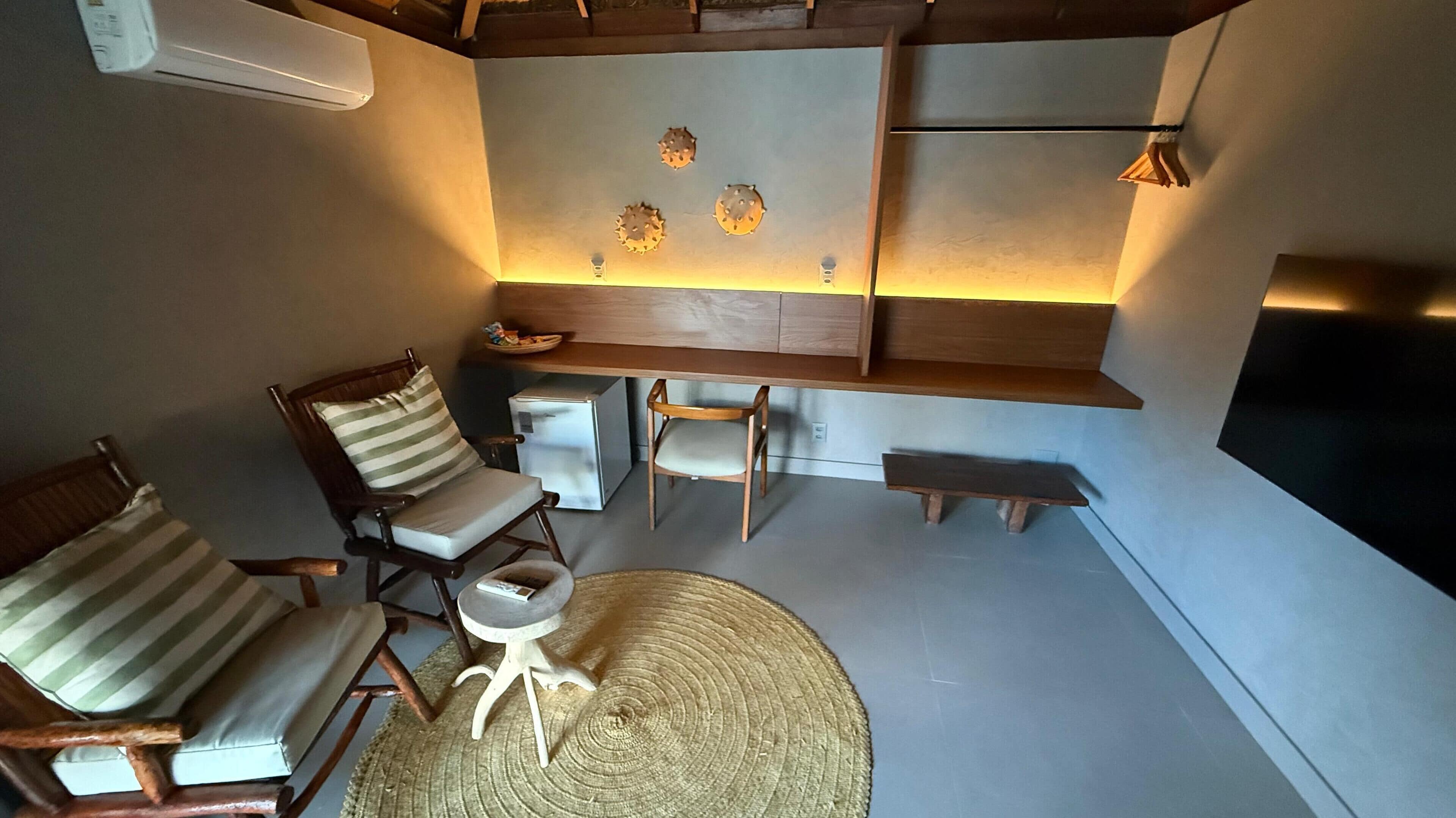 Una sala acogedora con techo de madera, televisor de pantalla plana, banca de madera y dos sillones con cojines.