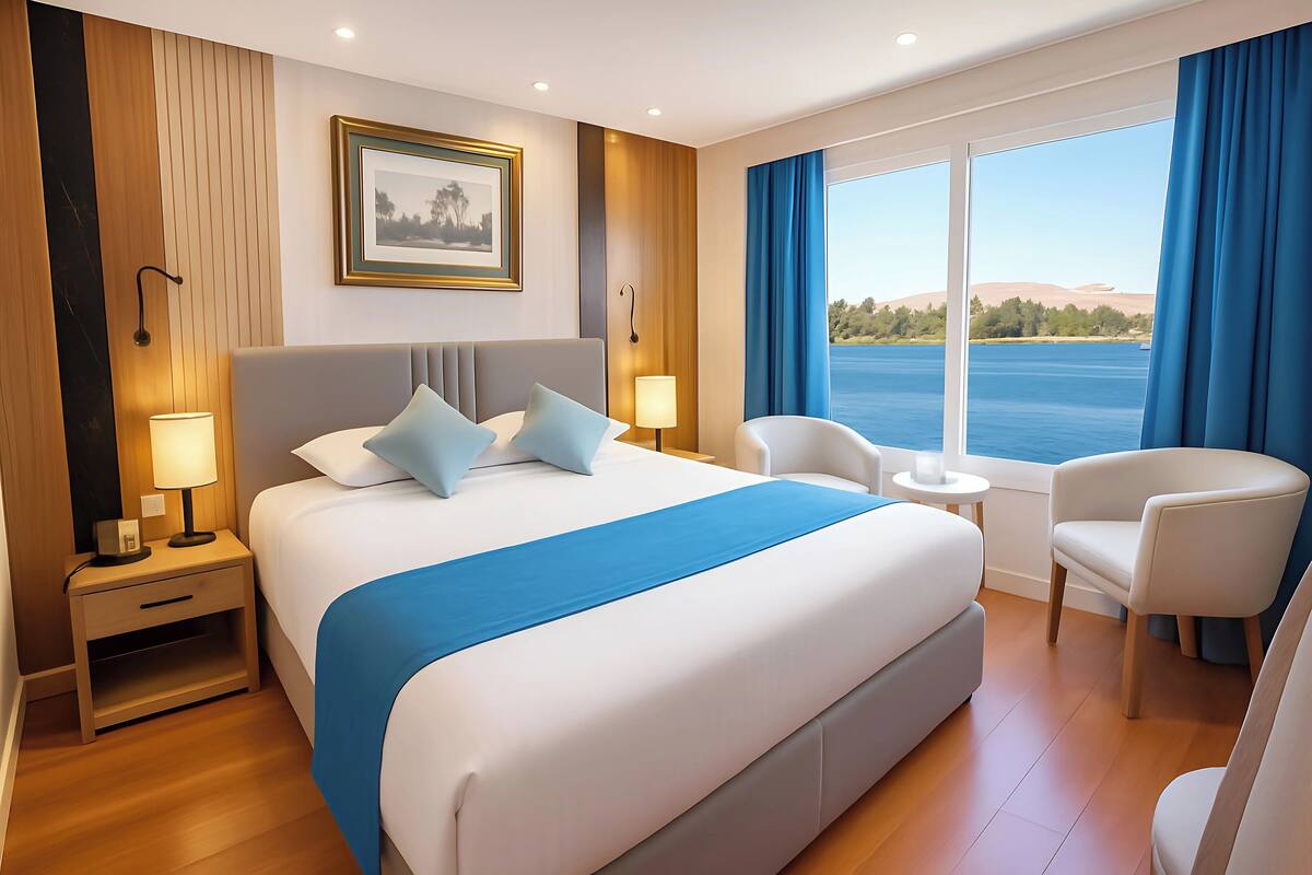 A modern hotel room with a large bed, a desk, two chairs, and a view of the water.