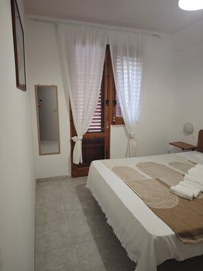 A bedroom with a bed, a wooden door, a mirror, and a window with curtains.