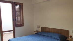 Ein Schlafzimmer mit einem Bett, einem Nachttisch, einer Lampe und einem Fenster mit Jalousien.