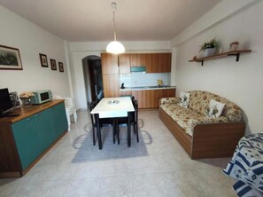 A compact living space with a dining table, sofa, kitchenette, and a ceiling light. - Martinella House - Residence Baia Renella (Sicilia)