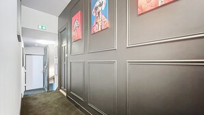 A hallway with grey walls, framed artwork, and a carpeted floor. - Appart Hôtel de la Baie  (Saint-Jean-le-Thomas)