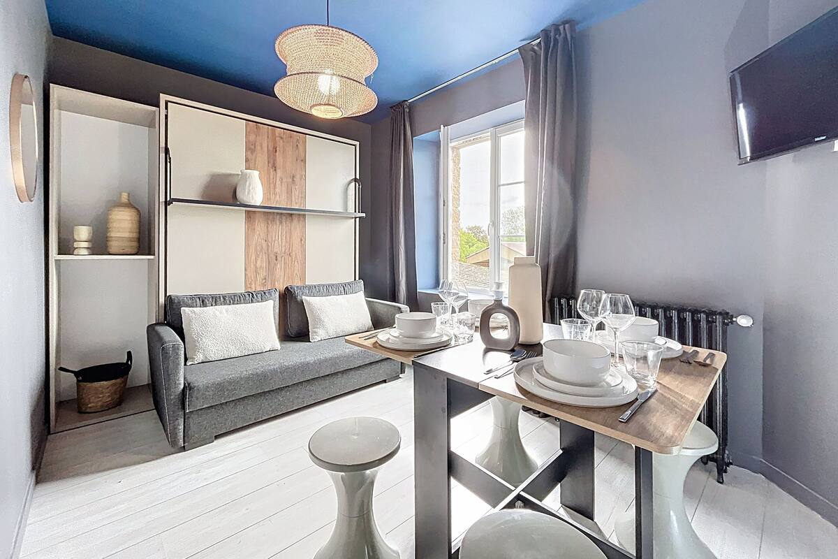 A modern living room with a sofa, a dining table set with plates and glasses, and a hanging light fixture.