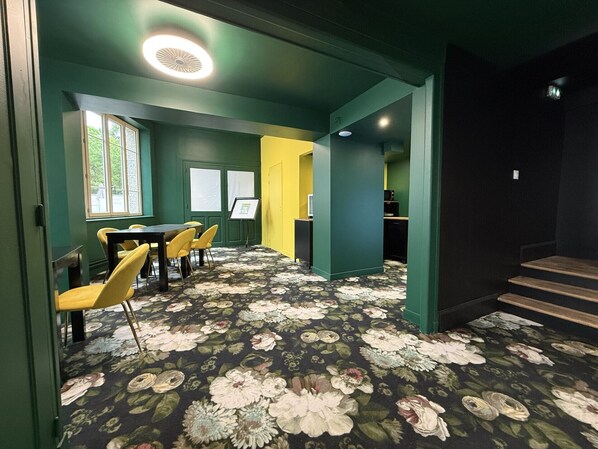 A room with a floral carpet, green walls, yellow chairs, a table, and a staircase. - Appart Hôtel de la Baie (Saint-Jean-le-Thomas)