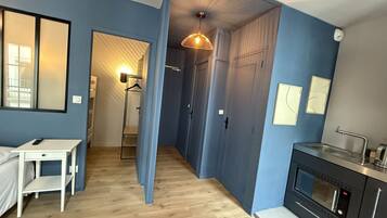 Un appartement moderne avec un mur d’accent bleu, un plancher en bois, une kitchenette équipée d’un four à micro-ondes et un luminaire suspendu.