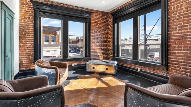 A room with a brick wall, large windows, leather chairs, a wooden floor, and a fur rug. - Apartment 2: Okmulgee Main St (Okmulgee)