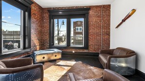 A room with leather chairs, a vintage radio, and a large window with a city view. - Apartment 2: Okmulgee Main St (Okmulgee)