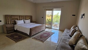 A bedroom with a large bed, a sofa, a nightstand, and a balcony with a table and chairs.