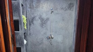 A bathroom with a toilet, two white mats, a shower, and a light fixture.