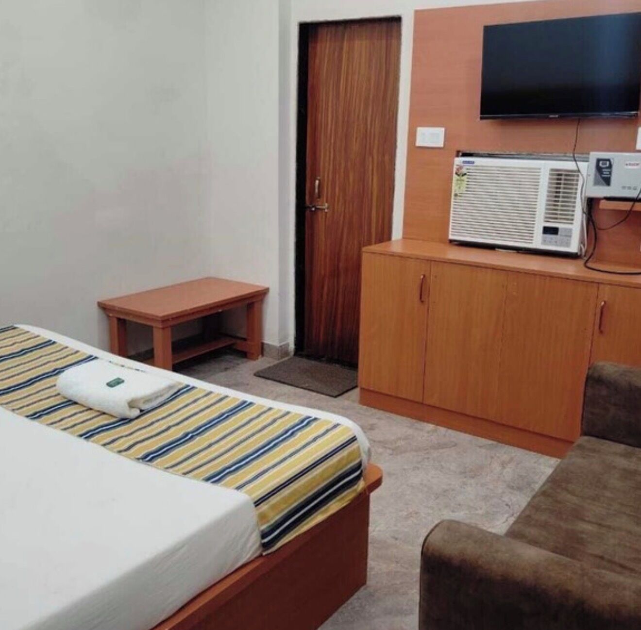 Habitación de hotel con cama, una mesita, armario, televisor y aire acondicionado.