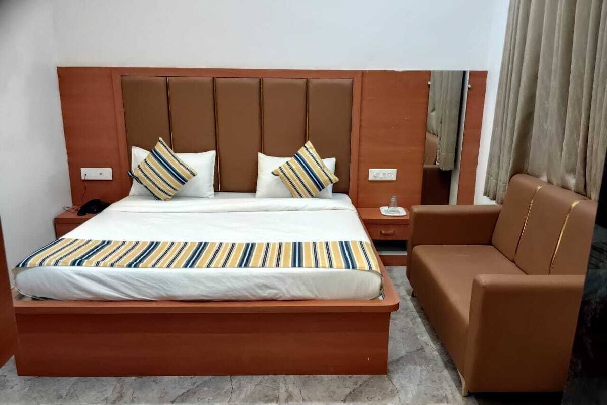 Una habitación de hotel con una cama grande, cabecera marrón, sofá marrón y piso de mármol.