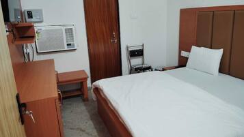 Una camera d'albergo con un letto, un armadio in legno, una panca, un condizionatore d'aria e una porta.
