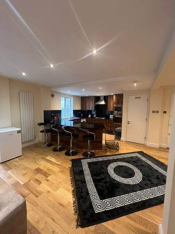 A modern kitchen with a central island, bar stools, and a black rug with a geometric pattern. - 3-bed Central Apartment - Sleeps 8 & Free Parking (London)