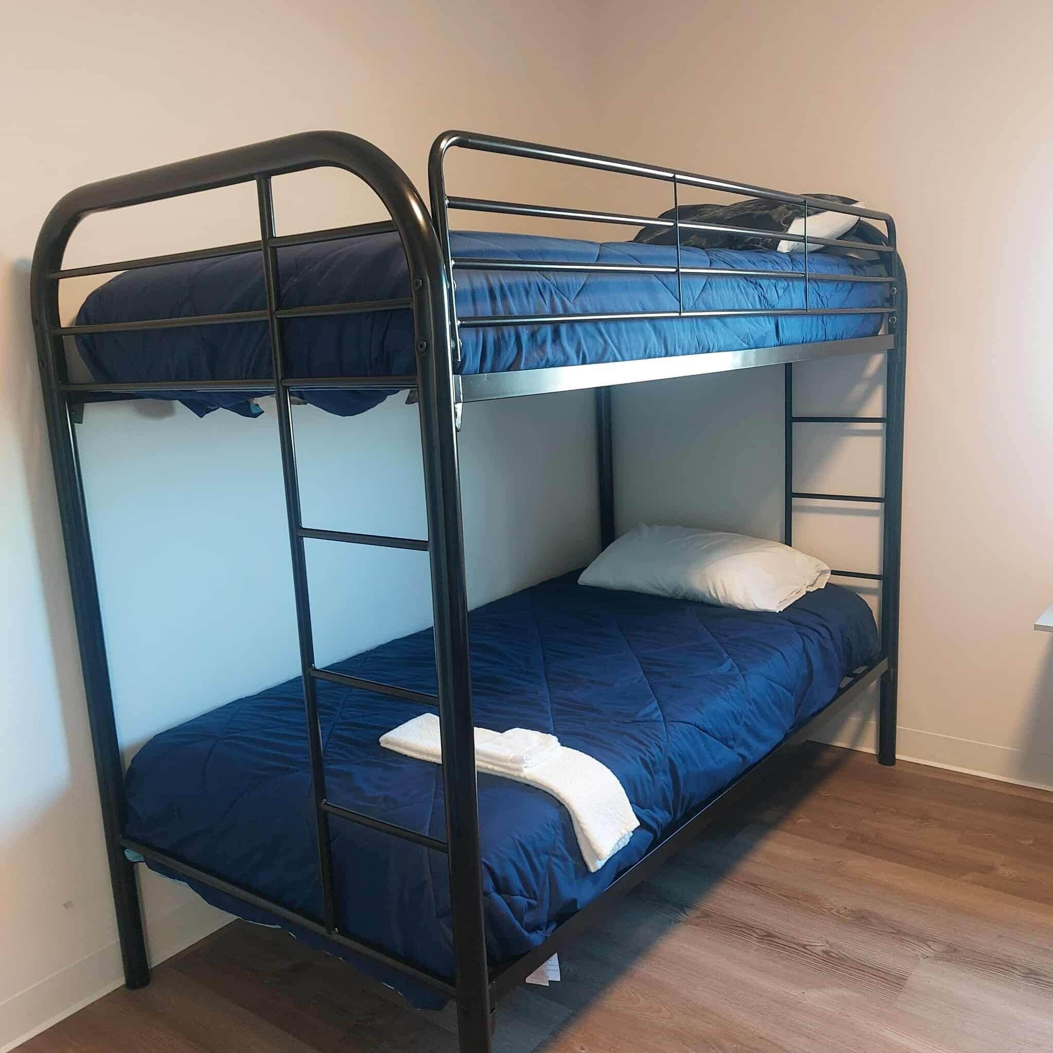 Una cama litera con ropa de cama azul y una almohada blanca en una habitación con suelo de madera.