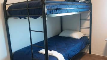 Una cama litera con ropa de cama azul y una almohada blanca en una habitación con suelo de madera.