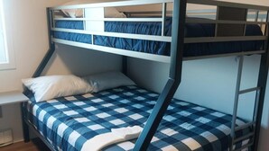 Ein Etagenbett mit einer blau-weiß karierten Decke, einem weißen Kopfkissen und einem Fenster links.