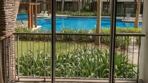 A modern hotel room with a large sliding glass door leading to a pool area with palm trees and a clear blue sky. - Exceptional apartment with a view of the golf course and beach—a 3-minute walk away (Grand Baie)