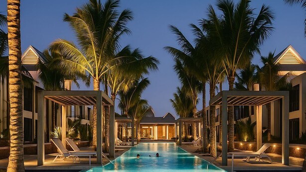 A swimming pool with a tiled surface, surrounded by palm trees and lounge chairs, with a building in the background. - Exceptional apartment with a view of the golf course and beach—a 3-minute walk away (Grand Baie)