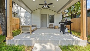 Une terrasse couverte avec un ventilateur de plafond, un barbecue et des sièges.