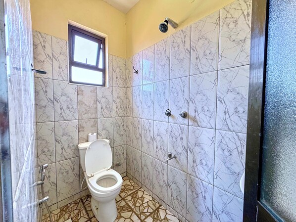 A bathroom with a toilet, a window, and a shower. - Goldstone Hotel (Tiwi)