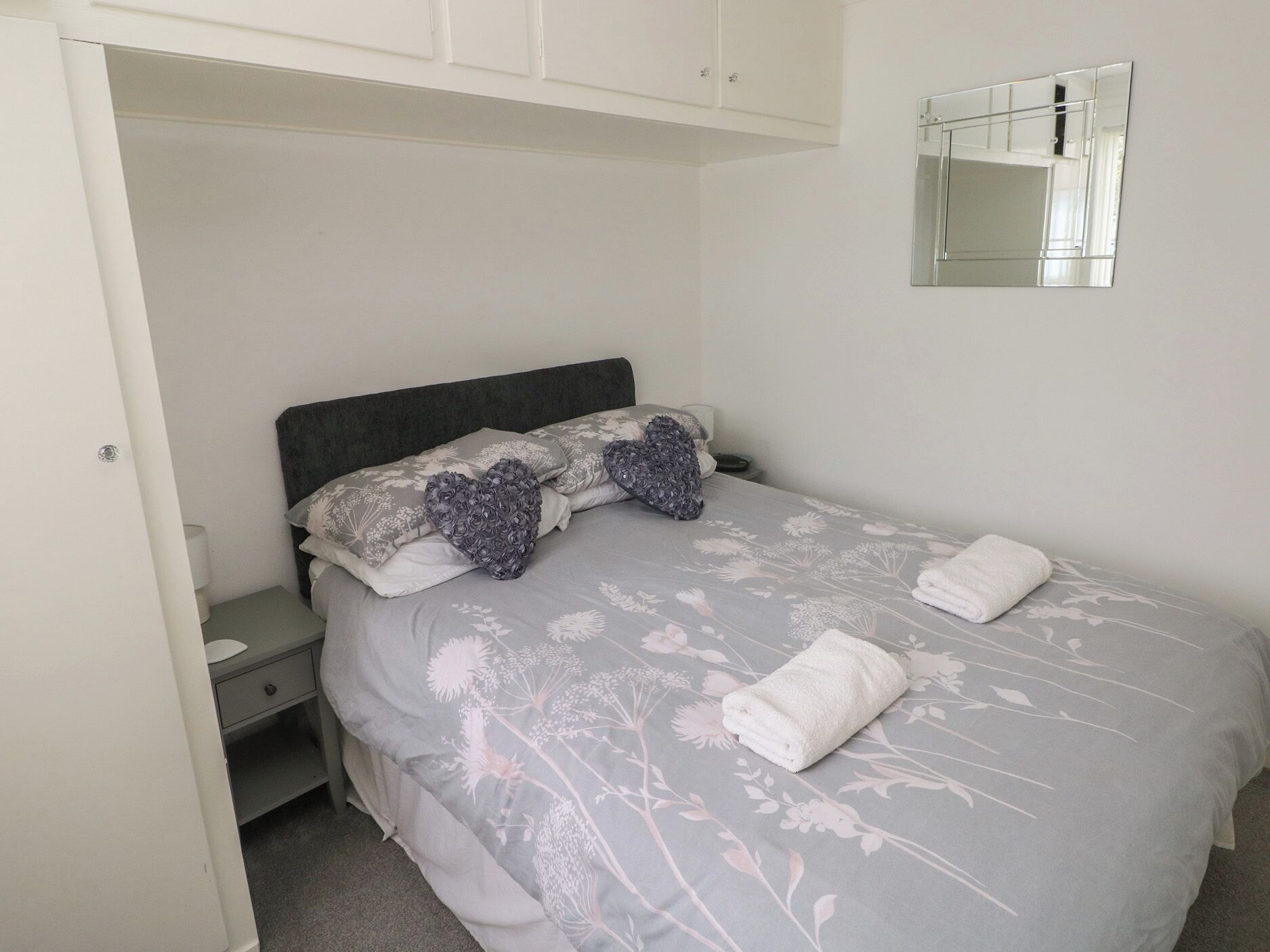 A bedroom with a bed, a bedside table, a nightstand, a mirror, and a wardrobe.