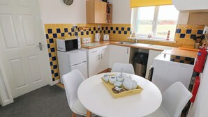 Une cuisine compacte équipée d’un four à micro-ondes, d’un grille-pain et d’un évier. On y trouve une table à manger avec des chaises et un plateau de nourriture.