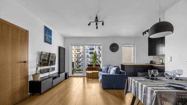 Een moderne woonkamer met een bank, televisie en een eethoek met een tafel gedekt voor vier personen.