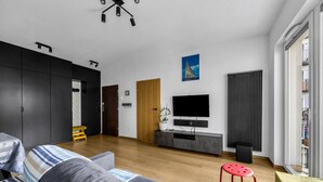 Een moderne woonkamer met een grijze bank, een rode kruk, een flatscreen televisie en een radiator.
