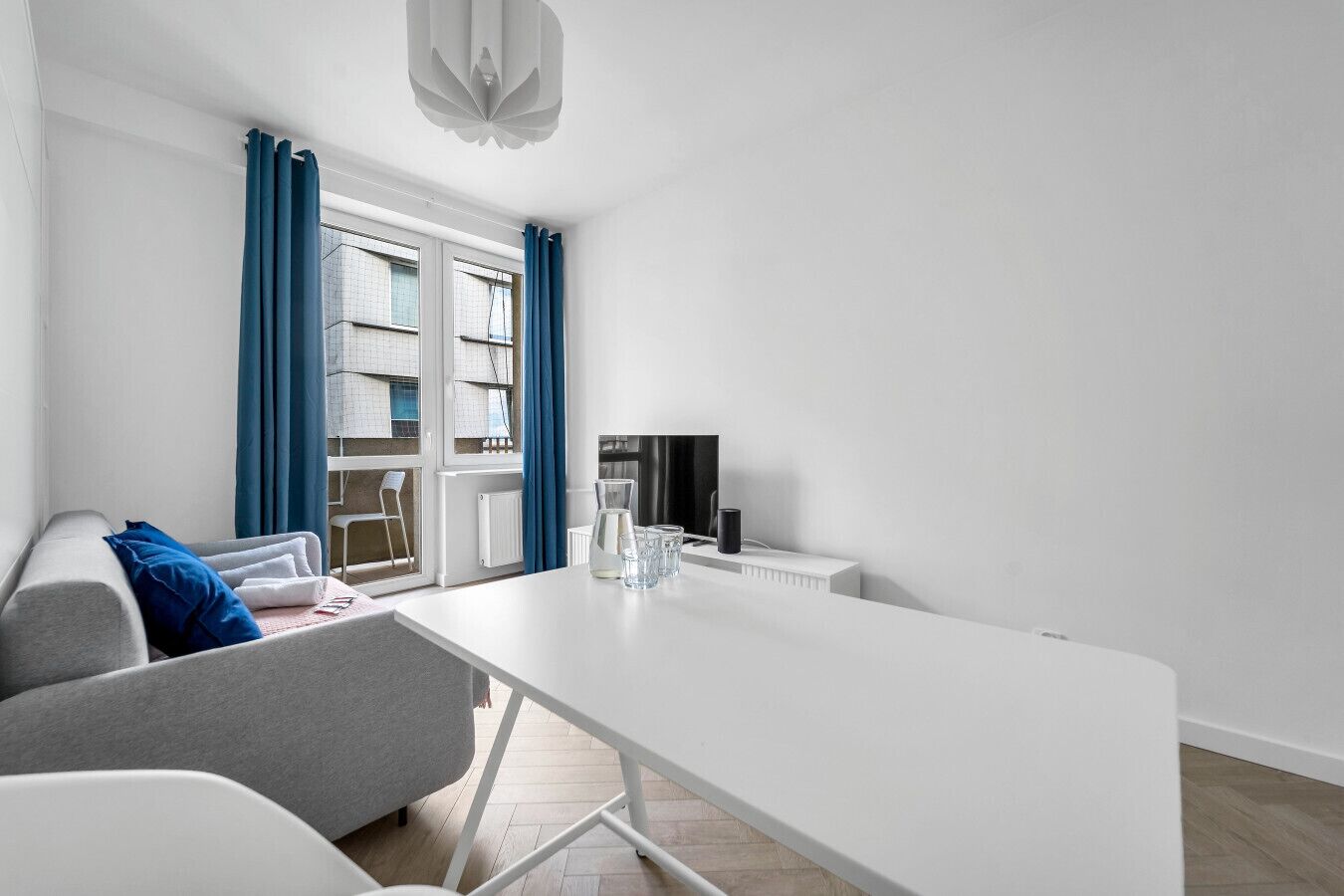 A modern living room with a white sofa, a dining table, and a TV.