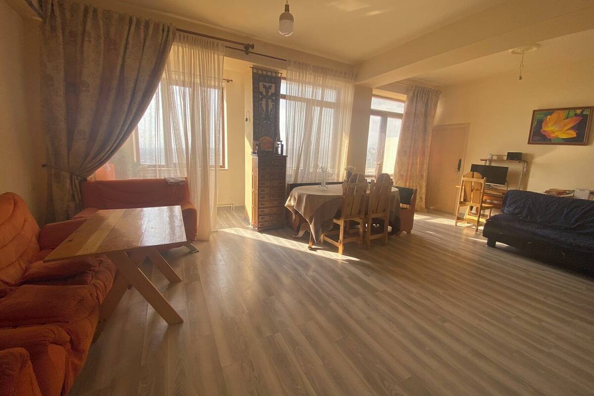 A spacious living room with a wooden floor, a dining area with a table and chairs, a sofa, and a TV.