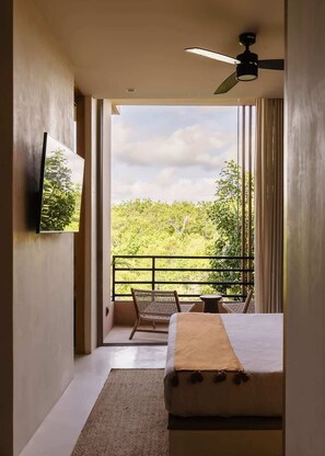 A bedroom with a bed, a ceiling fan, a TV, and a balcony with a view of greenery.