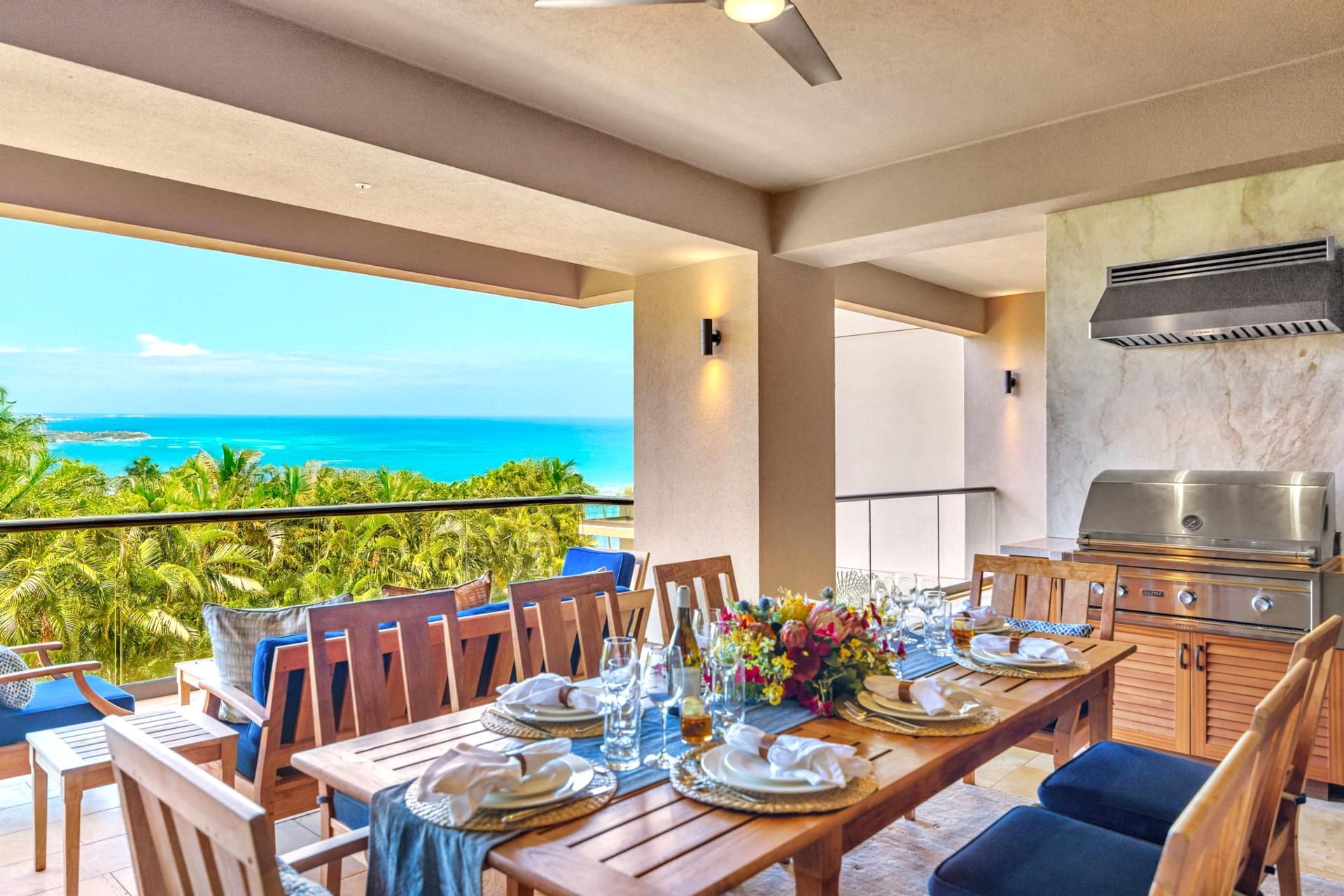 A dining area with a view of the ocean, a grill, and a table set for a meal.