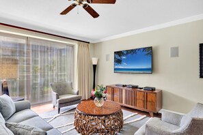 A living room with a sofa, armchair, round coffee table, TV, and a view of the outdoors through a sliding door. - Honua Kai | Ocean View 5 BR, Sleeps 14 | Car Incl. w/ 6+ Nights | HKK ML-1403 by KBM (Lahaina)