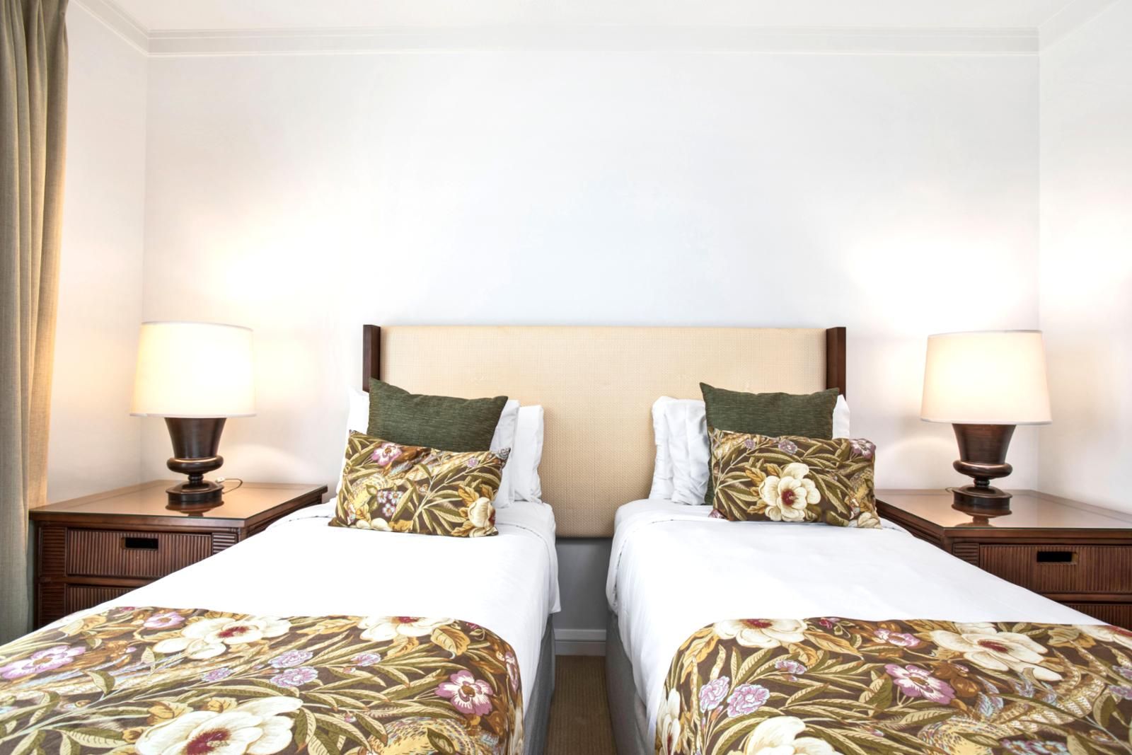 A hotel room with two beds, each with a floral bedspread and matching pillows, flanked by nightstands with lamps.