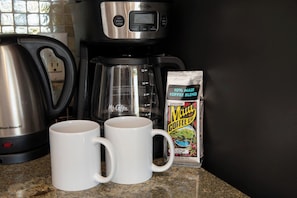 Una cocina con una cafetera Mr. Coffee, dos tazas blancas y una caja de café Mr. Coffee.