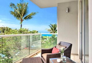 A balcony with a wicker chair, a small table, and a glass railing. - Honua Kai | Ocean View 5 BR, Sleeps 14 | Car Incl. w/ 6+ Nights | HKK ML-1403 by KBM (Lahaina)