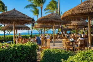 Ein Resort mit Reetdachschirmen, Holzstühlen und Blick aufs Meer.