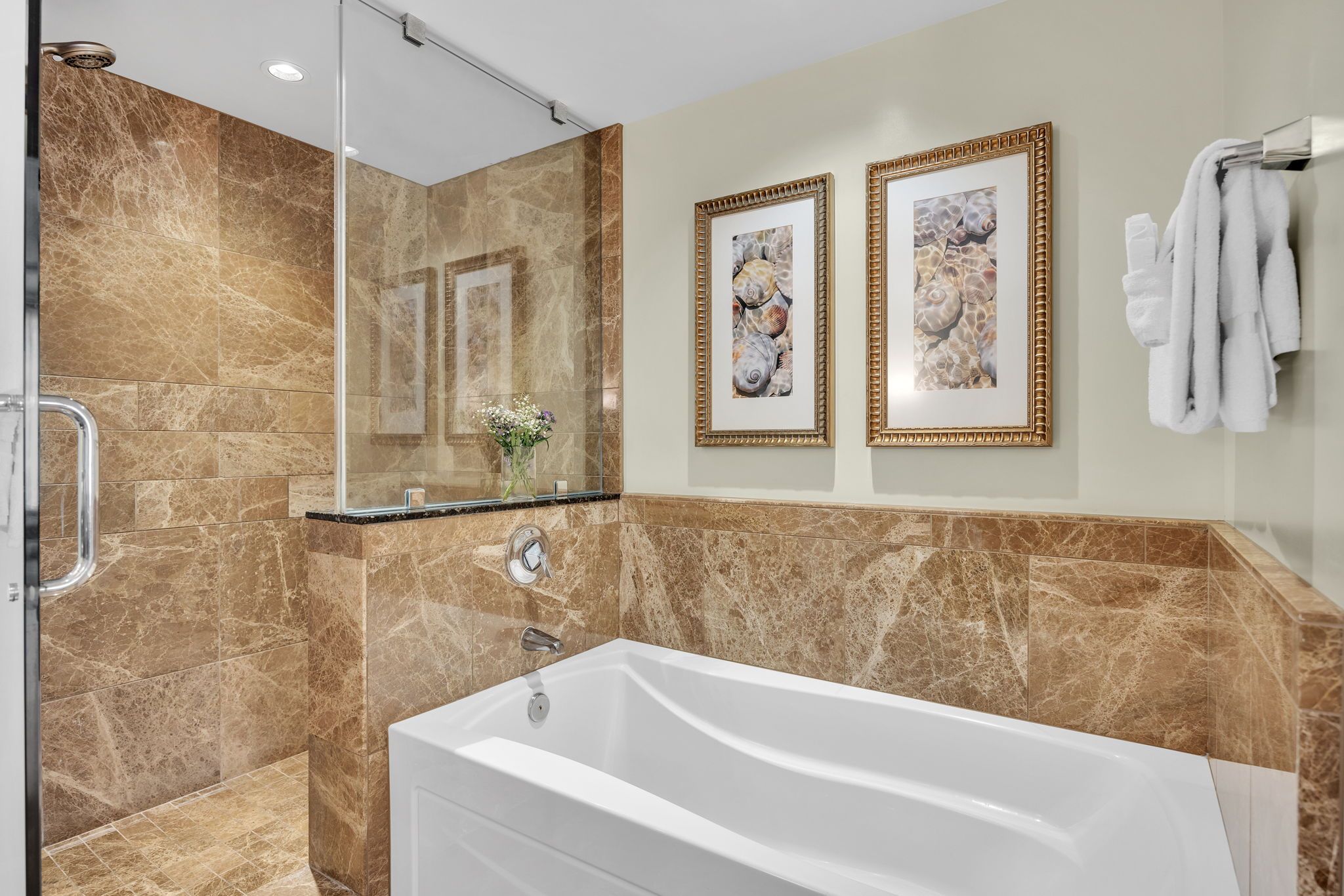 A modern bathroom with a glass shower enclosure, a freestanding bathtub, and two framed artwork on the wall.
