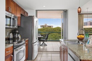 Una cucina moderna con elettrodomestici in acciaio inossidabile, un'area pranzo con tavolo e sedie, e un balcone con vista su una collina.