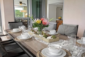 A dining table set with white plates, bowls, and glasses, a centerpiece with flowers, and a view of the outdoors.