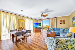 A room with a dining table, chairs, a sofa, a TV, and a ceiling fan.